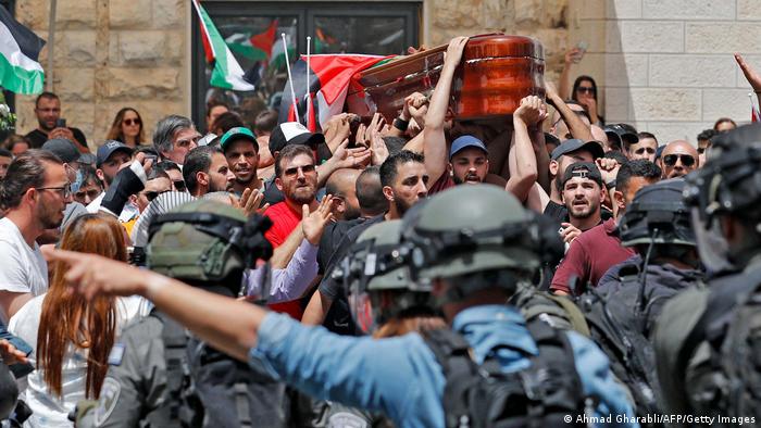 Sicherheitskräfte gegenüber einer Menge die, den Sarg trägt und Palästinensische Flaggen schwenkt