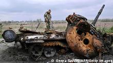 TOPSHOT - Ukrainian servicemen look at a destroyed Russian tank on a road in the village of Rusaniv, in the Kyiv region on April 16, 2022. - Many of the nearly five million people who have fled Ukraine will not have homes to return to, the United Nations said on April 16, 2022, as another 40,000 fled the country in 24 hours. (Photo by Genya SAVILOV / AFP) (Photo by GENYA SAVILOV/AFP via Getty Images)