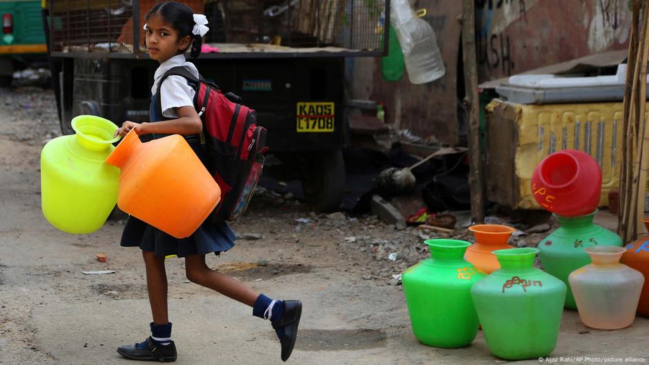 An Indian schoolgirl carries empty plastic vessels to fetch water from a shared tap