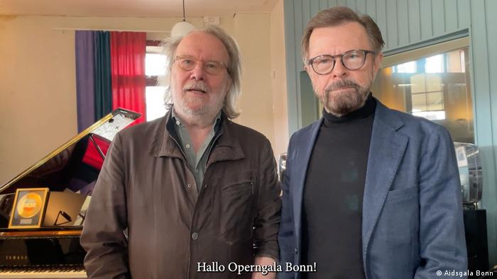 Björn Ulvaeus und Benny Andersson stehen nebeneinander und blicken in die Kamera, hinter ihnen ein Klavier 