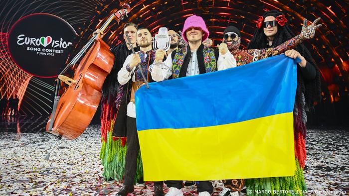 Members of the band Kalush Orchestra pose on stage with Eurovision winner's trophy and Ukrainian flag