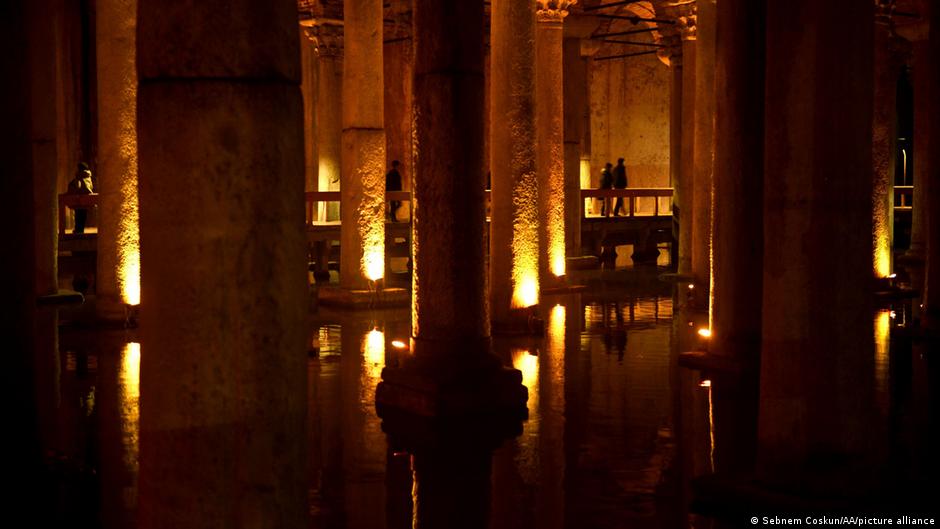 An underground view of the basilica Cistern in Istanbul, Turkey, with water covering the floor and columns holding up the ceiling, in the half dark