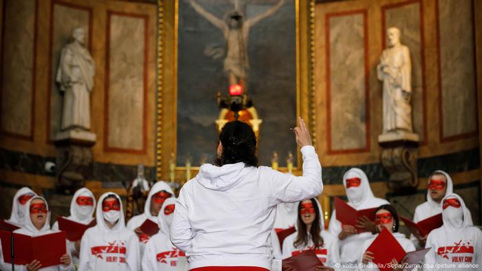 Учасники хору Volni в масках для очей співають перед церковним вівтарем під проводом жінки в білому худі