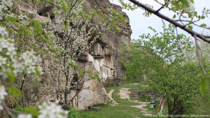 Monastère de Tipova creusé dans la roche avec des arbres en fleurs au premier plan.