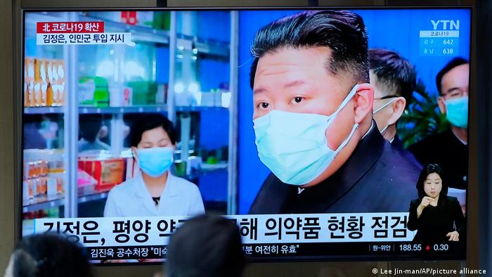 People watch a TV screen showing a news program reporting with an image of North Korean leader Kim Jong Un who blasted officials over slow medicine deliveries and ordered his military to respond
