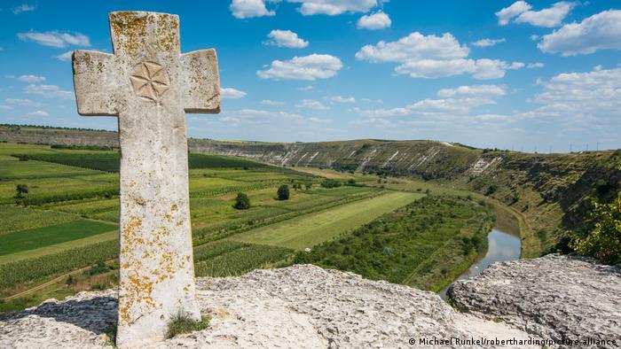 A cross on a stone in front of a green landscape and a river in the Orheiul Vechi.