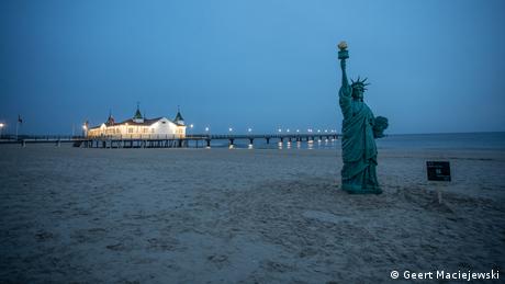 Beach with a statue of liberty, and a pier with lit buildings