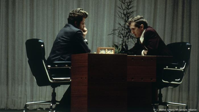 Boris Spasski und Bobby Fischer sitzen sich an einem Tisch gegenüber und spielen Schach.