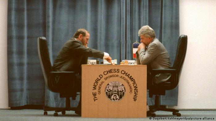 Bobby Fischer und Boris Spasski spielen gegeneinander 1992. Der Tisch, an dem sie sitzen, trägt die Aufschrift: The world chess championship.