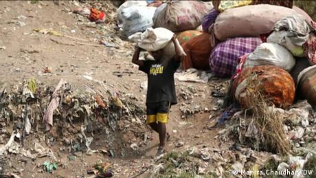 A man walks with a full bag on his head, amid the waste in a landfill site