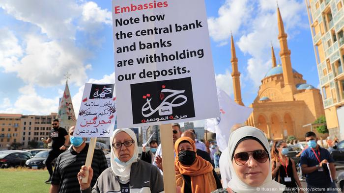 Lebanese depositors hold placards saying 'Note how the central bank and banks are withholding our deposits.'
