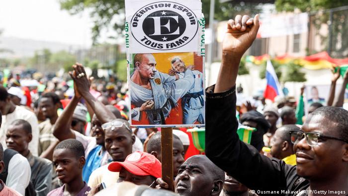 A supporter of Malian Interim President holds up a sign with the images of President of Russia Vladimir Putin kicking President of France Emmanuel Macron.