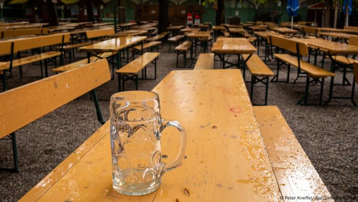 An empty beer mug on a table flanked by two benches; several similar tables are seen in the background