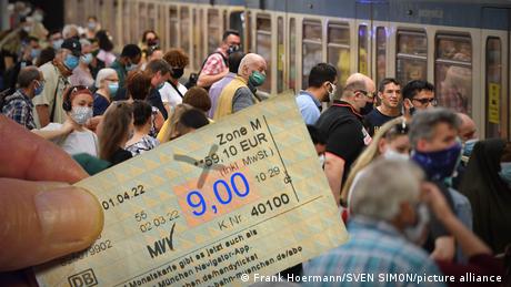 Viele Menschen stehen an einem Bahnsteig und steigen in einen Zug ein, jemand hält ein Neun-Euro-Ticket. (Frank Hoermann/SVEN SIMON/picture alliance)