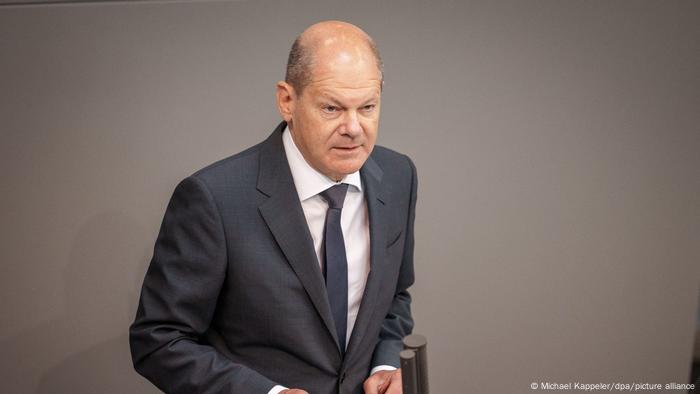 Olaf Scholz wears a grey suit and stands with slightly hunched posture