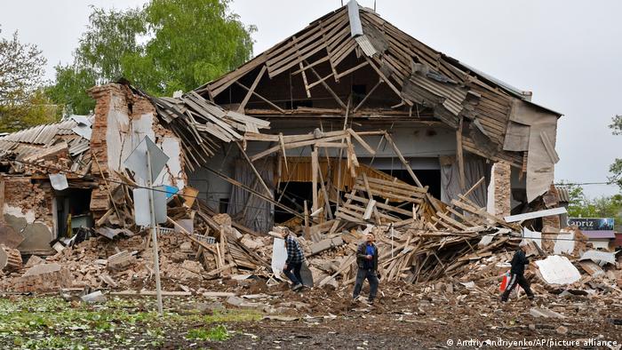 People walk past a destroyed house