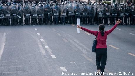 Female protester stands in front of row of police in 2021