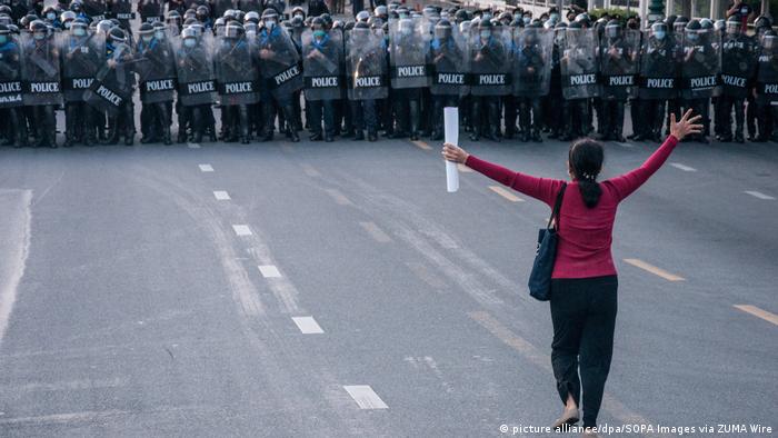 Female protester stands in front of row of police in 2021