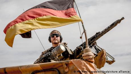  A Bundeswehr soldier is standing next to his machine gun and a German flag at the airport near the base in Gao, northern Mali