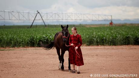 A girl poses for a picture with her horse near an agricultural field