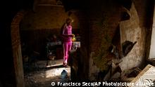A woman in a pink sweat suit stands out in the bombed out remains of her home