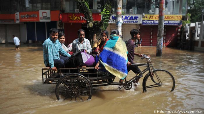 menschen Sitzen auf einem Fahrraddtransporter, in kniehohem Wasser. Bangladesch | Überschwemmung in Sylhet