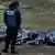 Ein Mensch mit einer Weste mit der englischen Aufschrift "Ermittler für Kriegsverbrechen blickt auch mehrere schwarze Leichensäcke, die nebeneinander aufgereiht liegen