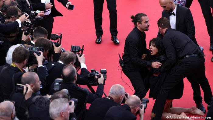 woman taken away on red carpet by men in suits