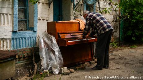 BdTD | Ukraine-Krieg Dorf Velyka Kostromka | Anwohner spielt Klavier vor beschädigtem Haus