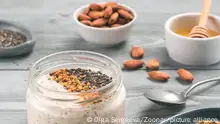 Overnight oats in jar and ingredients - chia seeds, almond, honey and pollen on gray wooden table background. Healthy breakfast oatmeal recipe idea