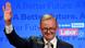 Anthony Albanese waves in front of a wall covered in his party's slogans Anthony Albanese waves in front of a wall covered in his party's slogans