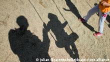Der Schatten von einem Mann, einem schaukelnden Flüchtlingsjungen und einem Flüchtlingsmädchen fallen am 27.08.2014 auf Sand auf einem Spielplatz in der Landesaufnahmebehörde Niedersachsen in Braunschweig (Niedersachsen). Die wachsende Flüchtlingszahl stellt immer mehr Kommunen in Niedersachsen vor Probleme. Insbesondere in den großen Städten und bevölkerungsreichen Landkreisen gibt es Schwierigkeiten bei der Unterbringung von Flüchtlingen. Foto: Julian Stratenschulte/dpa ++
