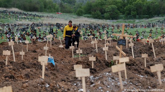 People stand amid newly-made graves at a cemetery in the course of Ukraine-Russia conflict in the settlement of Staryi Krym outside Mariupol