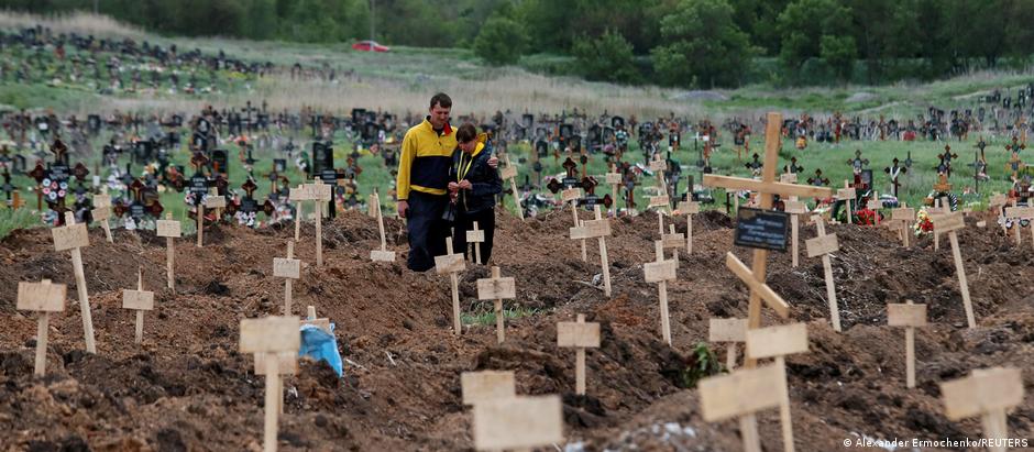 People stand amid newly-made graves at a cemetery in the course of Ukraine-Russia conflict in the settlement of Staryi Krym outside Mariupol