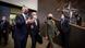 Two men in blue suits and one in a green Russian army uniform, all wearing face masks, walking into a room with the NATO symbol on the wall behind them. Two men in blue suits and one in a green Russian army uniform, all wearing face masks, walking into a room with the NATO symbol on the wall behind them.