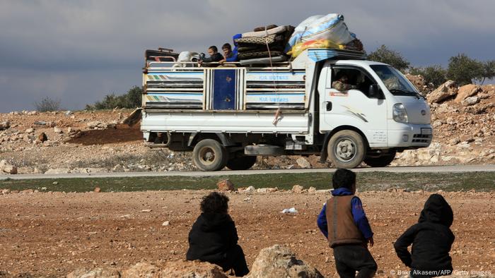 Children watch as a truck transports internally displaced Syrians to a new housing complex