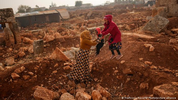 A Syrian woman holds a child next to ancient Roman era ruins where they have set their tents in Sarmada district, north of Idlib city, Syria, on Nov. 25, 2021