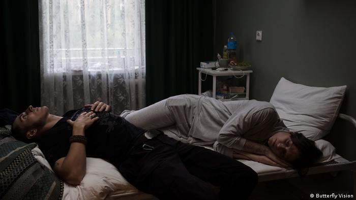 Кадр из фильма «Видение бабочки»: два человека лежат на кровати головами в разные стороны.