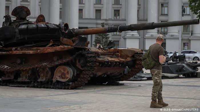 A man in camouflage uniform looks at a destroyed Russian tank