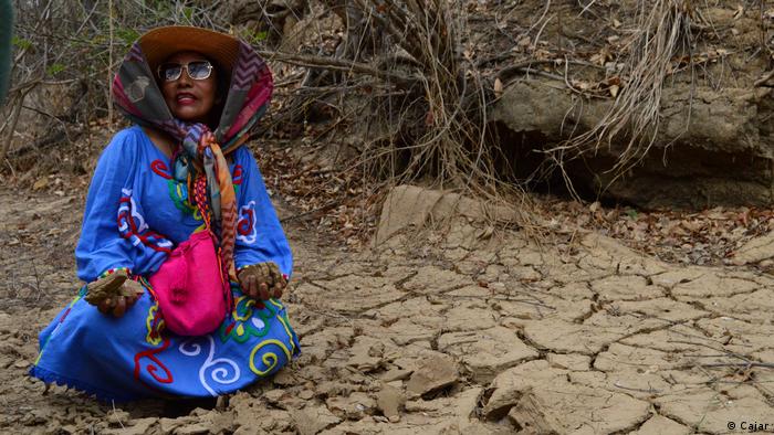 Indigenous woman sitting on dry, cracked ground