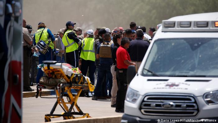 People and responders are seen standing next to an ambulance
