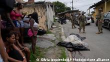 11.02.2022
Women watch as military police patrol where the covered body of a person, who was killed during a police operation, lies in the street in the Vila Cruzeiro favela in Rio de Janeiro, Brazil, Friday, Feb. 11, 2022. The police operation against alleged drug traffickers left at least eight people dead. (AP Photo/Silvia Izquierdo)