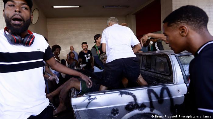 Men gather around the injured in the back of a pick up truck with spray paint on it