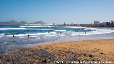 Der Stand Las Canteras auf Las Palmas de Gran Canaria, Spanien. Einige Leute sind im Wasser, auch mit Surfbrettern, unterwegs.