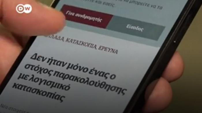 A hand holding a smartphone, reading an online report written in Greek