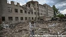 A woman walks past a destroyed administration building in the city of Bakhmut in the eastern Ukranian region of Donbas, on May 25, 2022. (Photo by ARIS MESSINIS / AFP) (Photo by ARIS MESSINIS/AFP via Getty Images)
