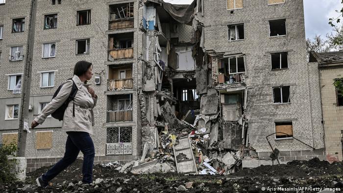 Una mujer pasa por delante de un edificio en ruinas. Una parte se ha derrumbado y yace amontonada en el suelo.