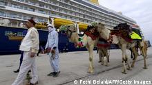 TOPSHOT - Tunisian men lead camels on March 23, 2022 at the port of La Goulette in Tunis as Tunisia welcomes the first cruise from Europe, with more than 800 tourists on board, after a stop recorded since 2019 due to the Covid-19 pandemic. - Tunisia expects to welcome a total of 44 cruises during the year 2022, recalling that in 2010, Tunisia welcomed 1 million tourists coming in cruises . (Photo by FETHI BELAID / AFP) (Photo by FETHI BELAID/AFP via Getty Images)