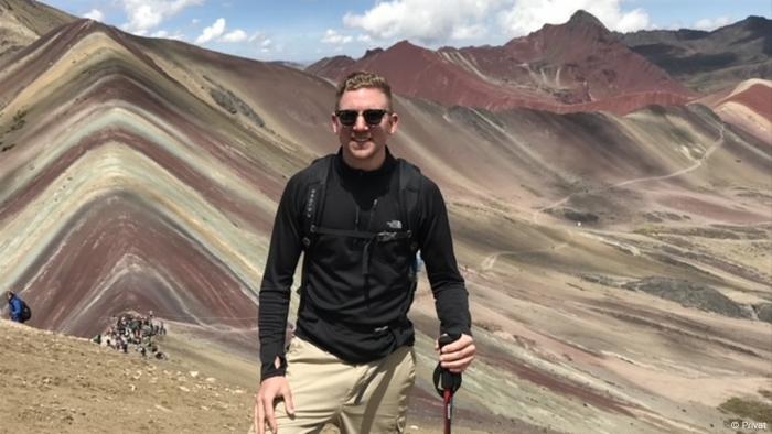 Todd Smith standing on one of the peaks of the multicolored 'Rainbow Mountain'
