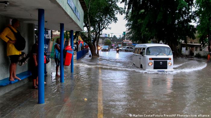 A woman stands on a bus stop bench as a driver of a Volkswagen van navigates a flooded street in Recife, state of Pernambuco, Brazil. (AP Photo/Marlon Costa/Futura Press)